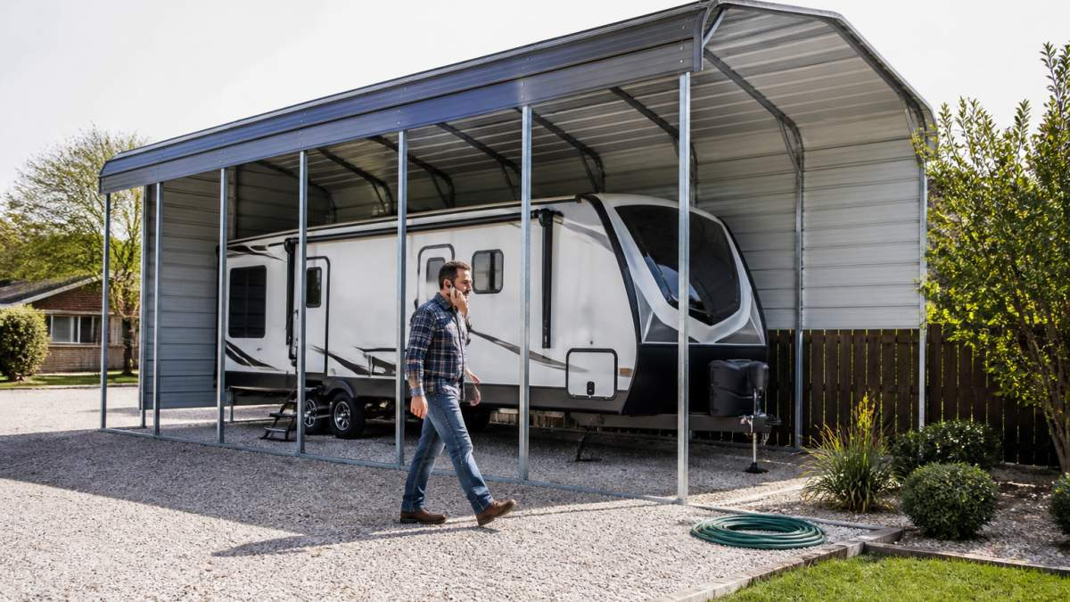 Owner inspecting a travel trailer under a steel carport to learn how to protect RV from sun damage.