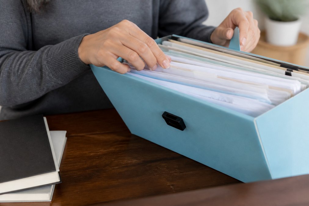 Close-up of hands organizing documents and files in a folder, showing record-keeping and documentation with natural lighting