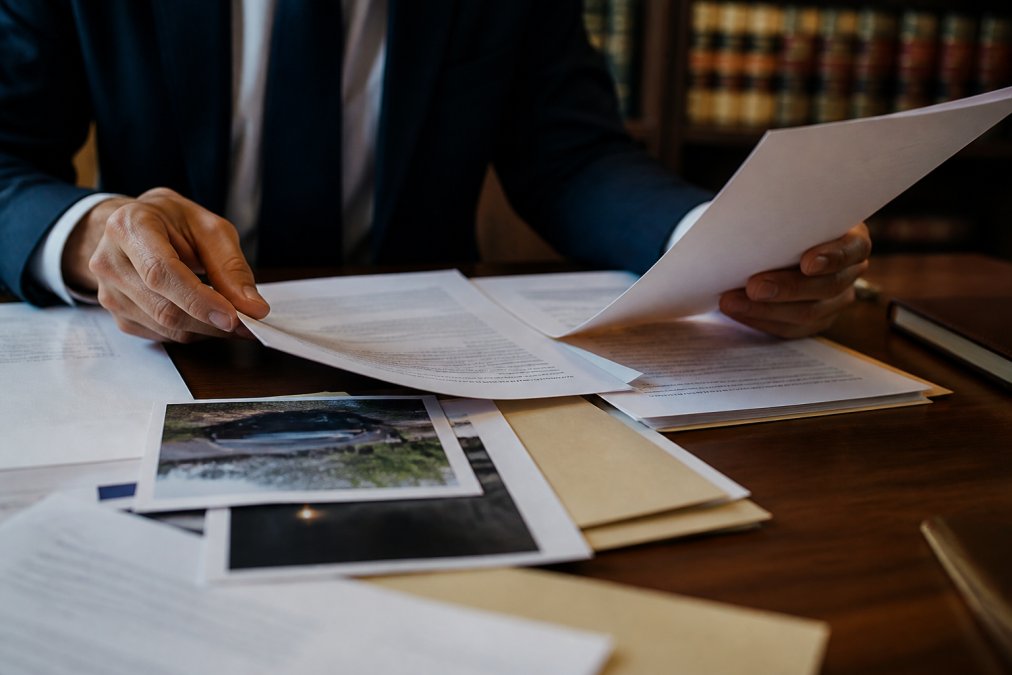 Close-up of hands organizing witness statements, photographs, and legal documents on a table in a law office setting