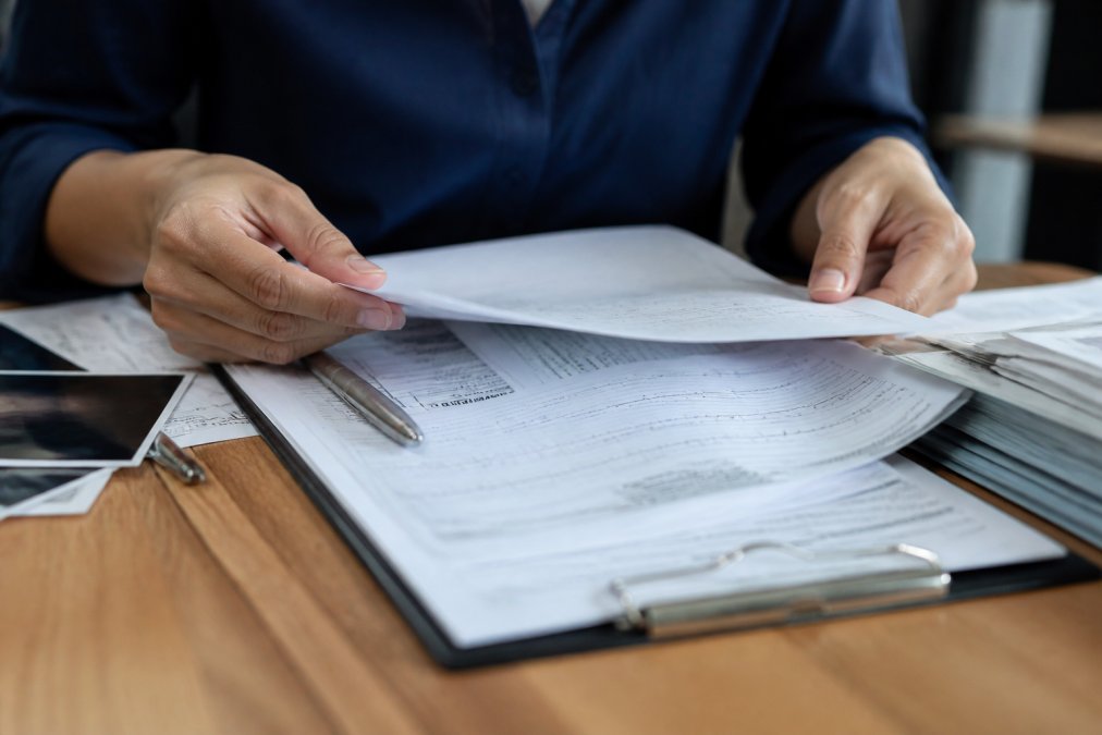 Close-up of hands organizing medical records and documents on a table with clipboard and pen for accident claim preparation