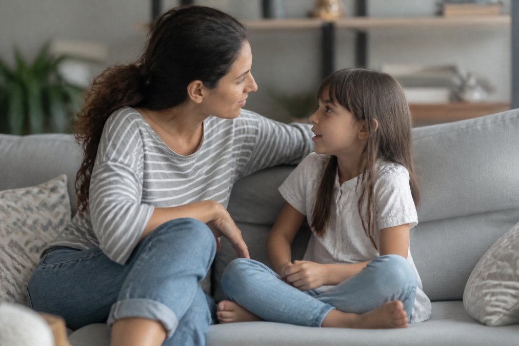 Parent and child sitting together on a couch having a warm, engaged conversation, showing active listening and emotional connection with natural home lighting
