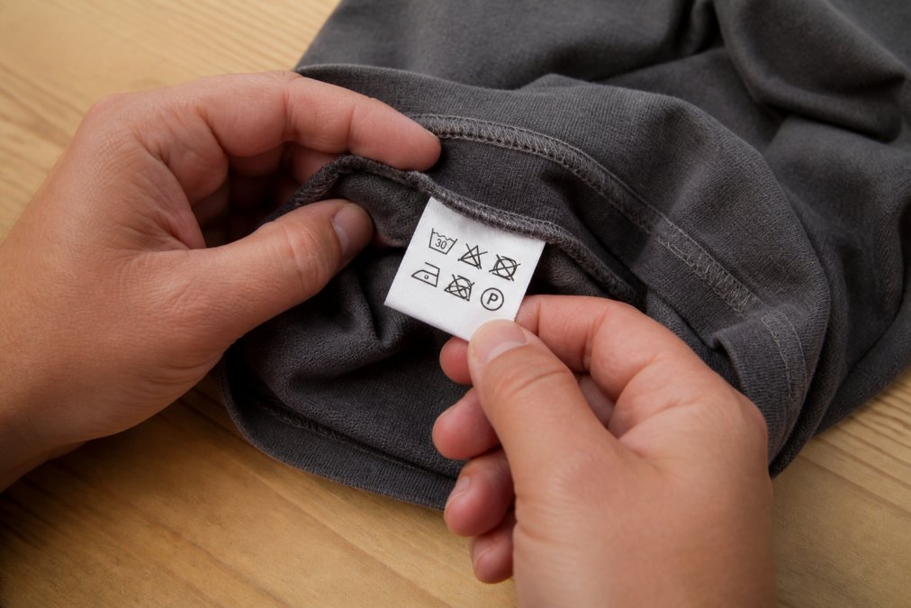 Close-up of hands identifying laundry care labels on a cotton garment seam to explain the washing symbol process