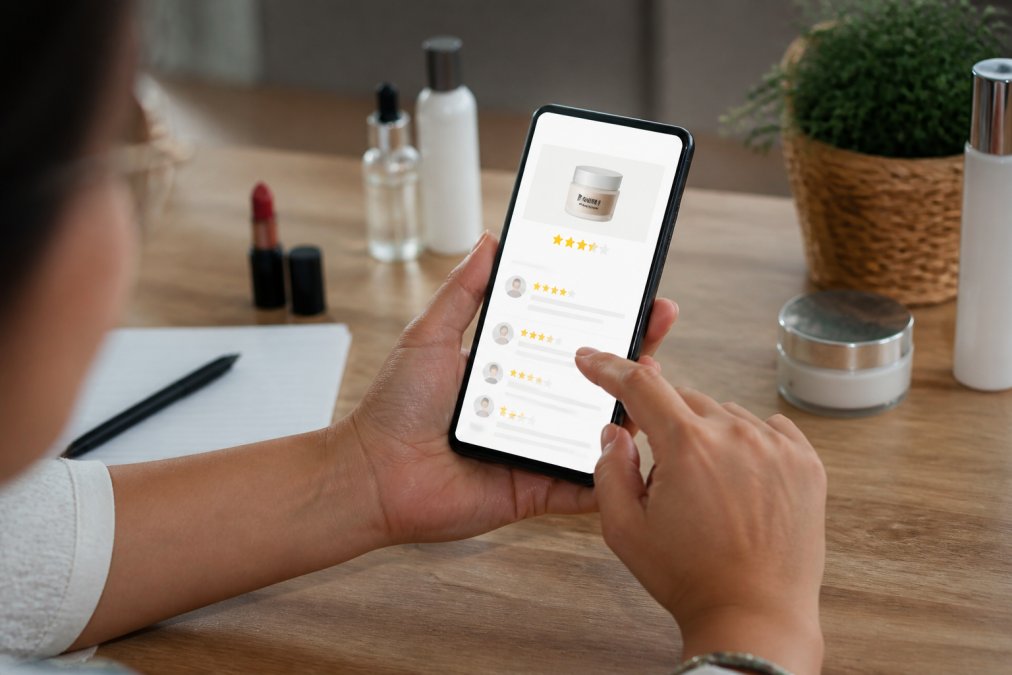 Close-up of hands holding a smartphone displaying customer reviews and star ratings on a beauty product page, with fingers scrolling through feedback