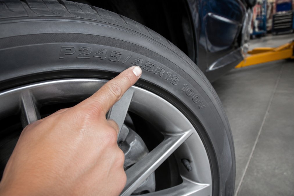 A person pointing at embossed sidewall markings to learn how to read tire size and speed rating on a car tire.