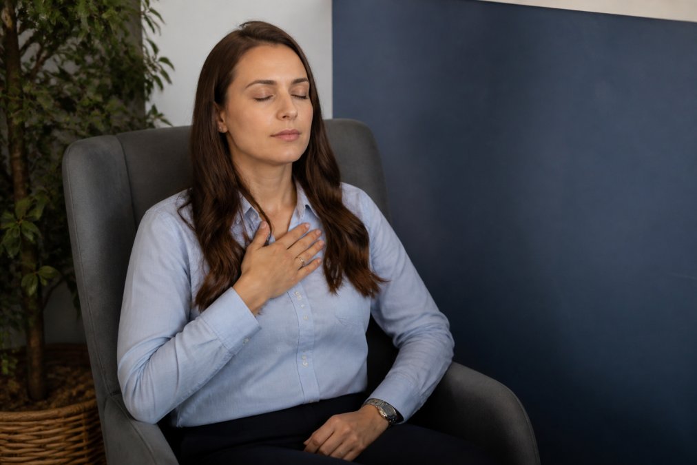 A professional taking a deep breath with eyes closed in a quiet office corner, hand on chest, practicing self-regulation before responding to feedback
