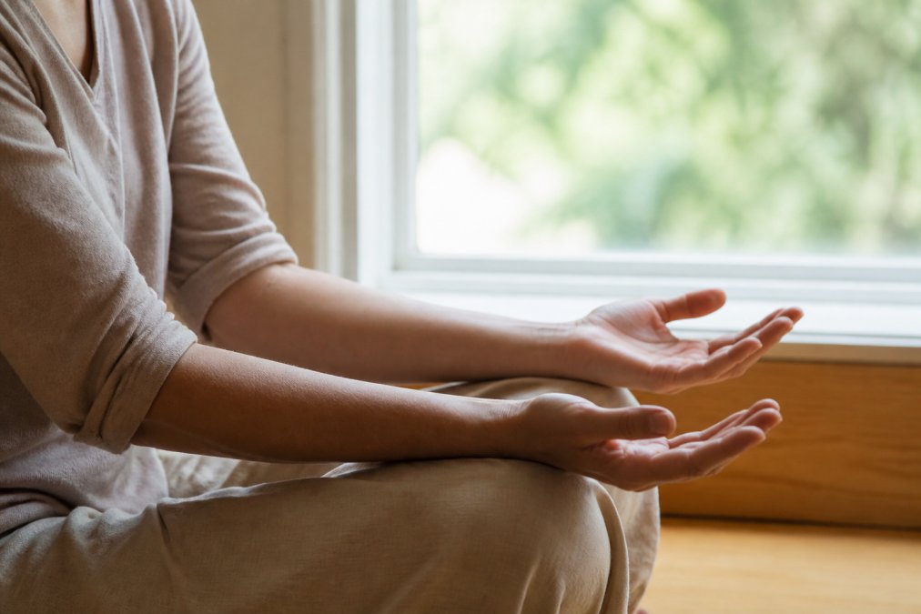 Close-up of a person's hands resting open and relaxed on their lap, palms facing upward, soft natural light coming through a window beside them, conveying stillness and gentle presence