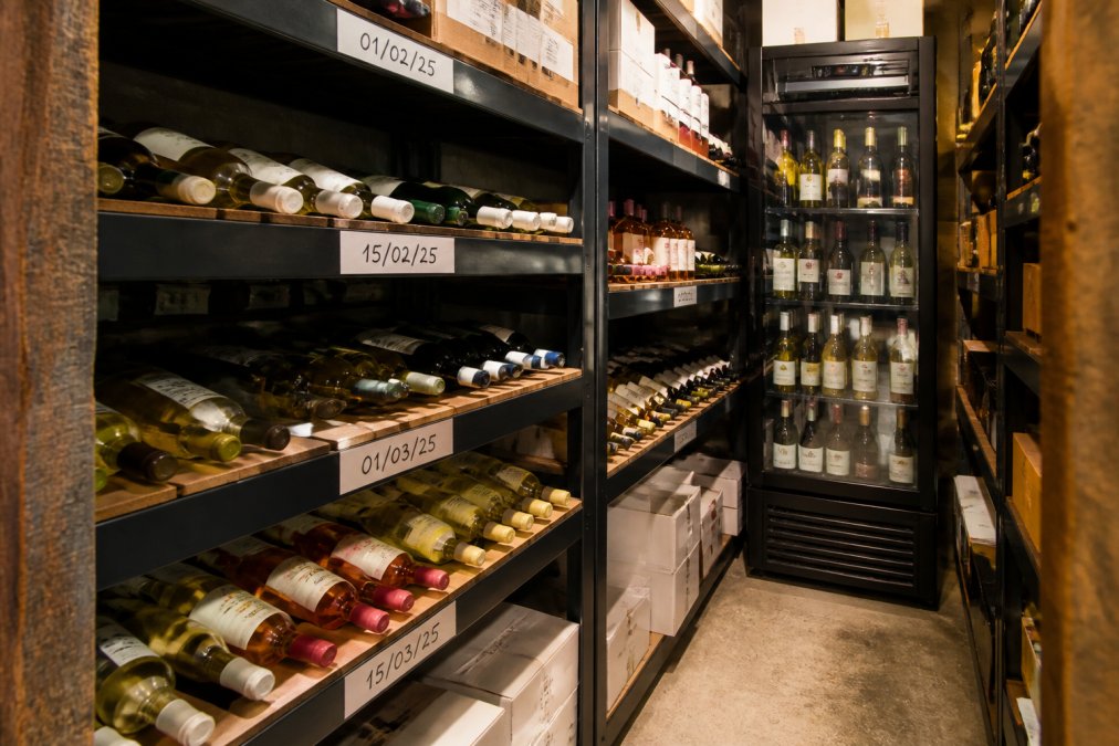 Organised pub cellar with drinks neatly stacked on shelves, clear date labels visible on bottles, stock arranged in logical rows with older stock positioned at front
