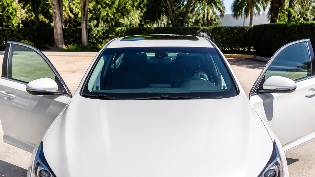 Person opening both front doors wide on a sunny day with windows rolled down, demonstrating proper ventilation technique to release hot air from vehicle cabin