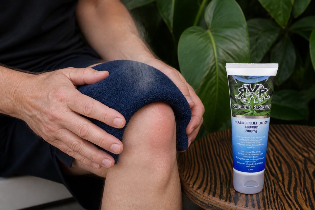 Close-up of hands applying a warm compress to a visibly swollen knee joint, with steam rising slightly from the compress on pale skin
