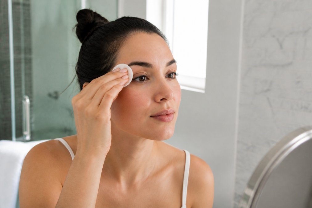 Woman gently cleansing her brow area with a cotton pad to help reduce pain during eyebrow waxing