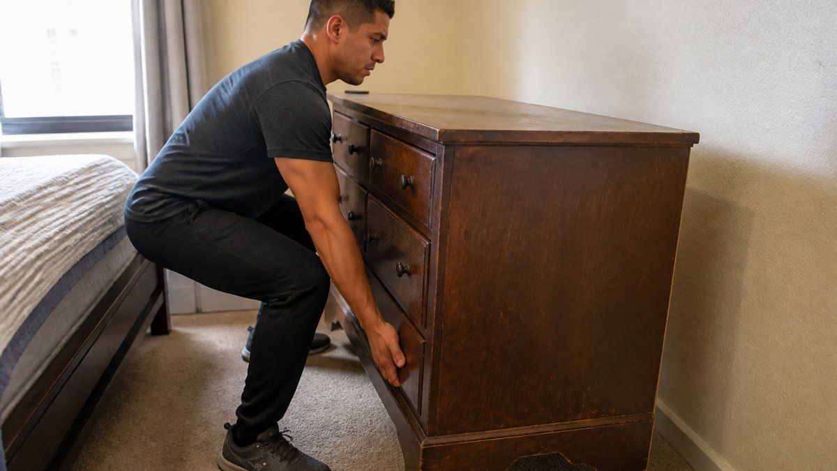 Person lifting a heavy wooden dresser with bent knees and a straight back to learn how to remove a heavy dresser safely.