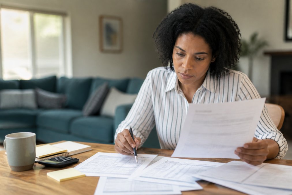 Person sitting at a desk reviewing printed credit report documents with a pen in hand, focused expression, natural home office lighting