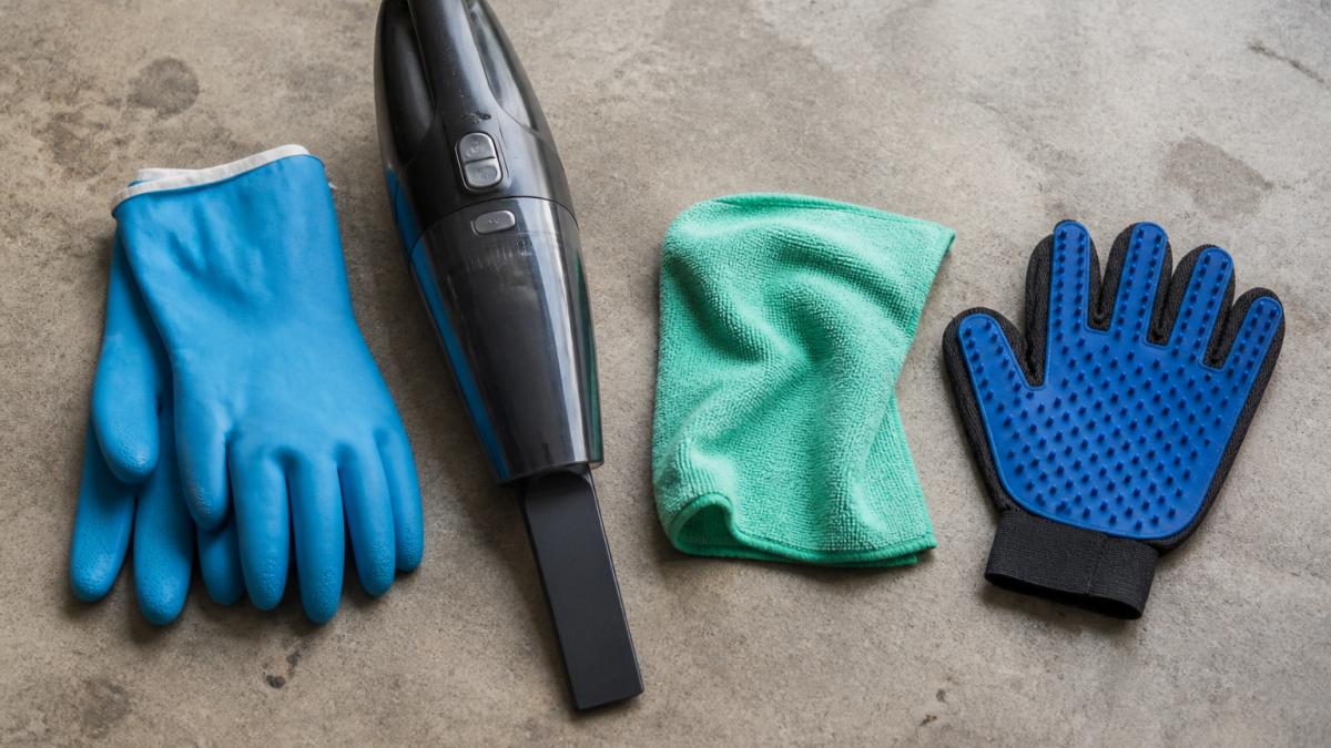Rubber gloves, a vacuum, and microfiber cloths arranged on a garage floor for cleaning pet hair