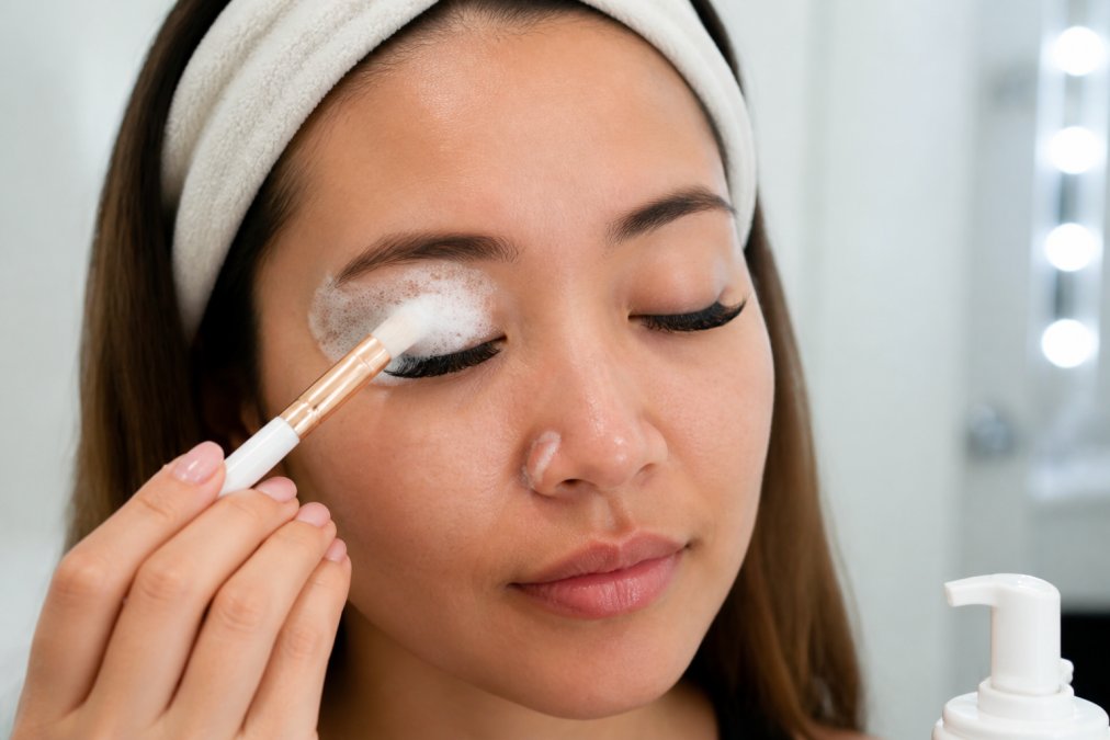 Woman gently cleansing her eye area with a foaming wash and soft brush to protect her lash extensions