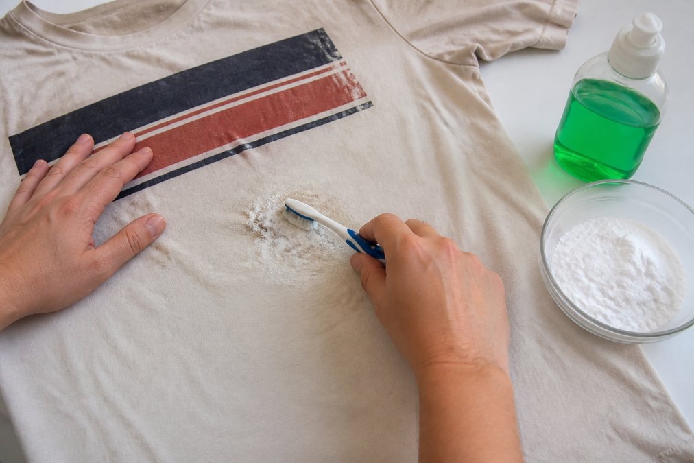 Scrubbing an oil stain on a cotton graphic tee with baking soda paste and a soft toothbrush