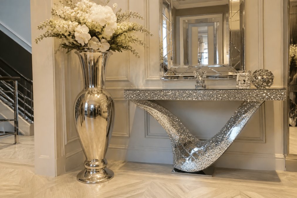 Elegant entryway with a large sculptural metal floor vase featuring vintage American-style silhouette and lustrous metal finish, positioned beside a crushed diamond mirror console table creating visual drama and architectural interest at the entrance, warm accent lighting