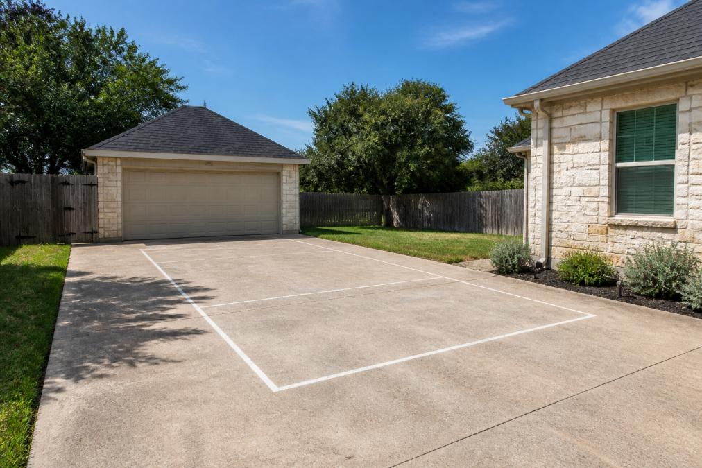 Residential driveway with clear, level surface and marked placement area for roll-off dumpster, showing no overhead obstacles or power lines visible