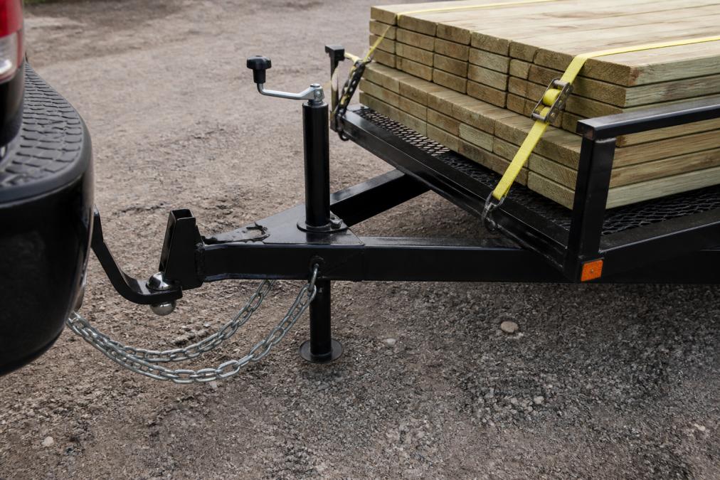 Close-up view of properly connected hitch ball mount with safety chains attached and secured cargo straps tightened across a loaded utility trailer bed