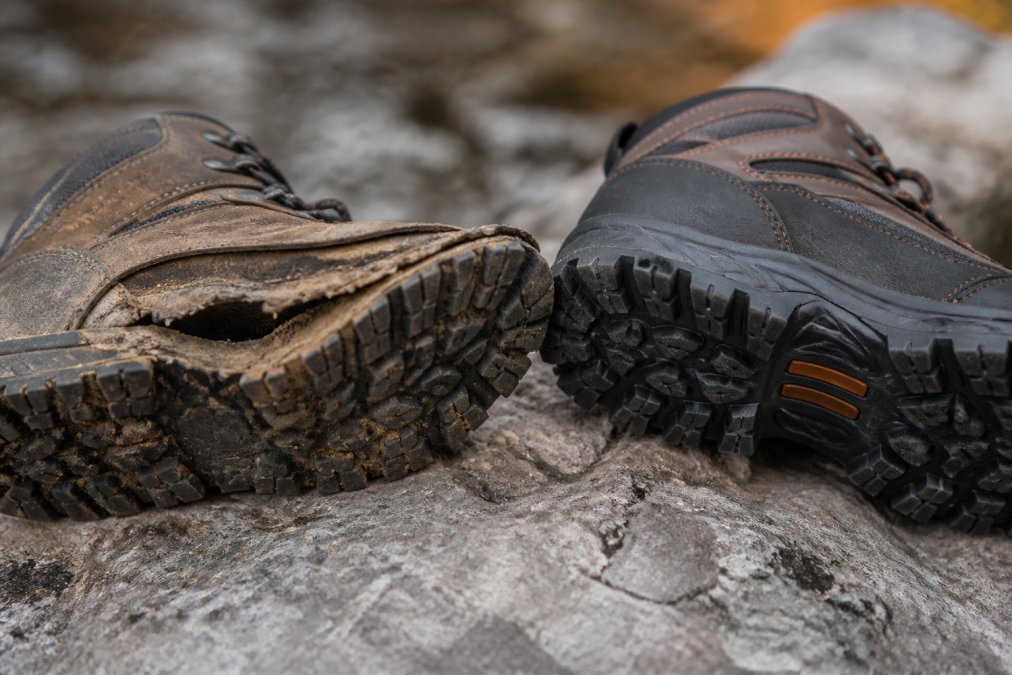 Close-up of worn hiking boot sole with visible separation and deteriorated tread pattern, next to a newer boot showing intact tread and firm sole attachment