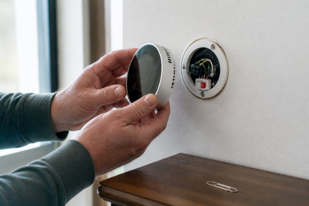 Diagram showing how to remove a wall-mounted smart thermostat cover to access the reset button and reset smart thermostat.