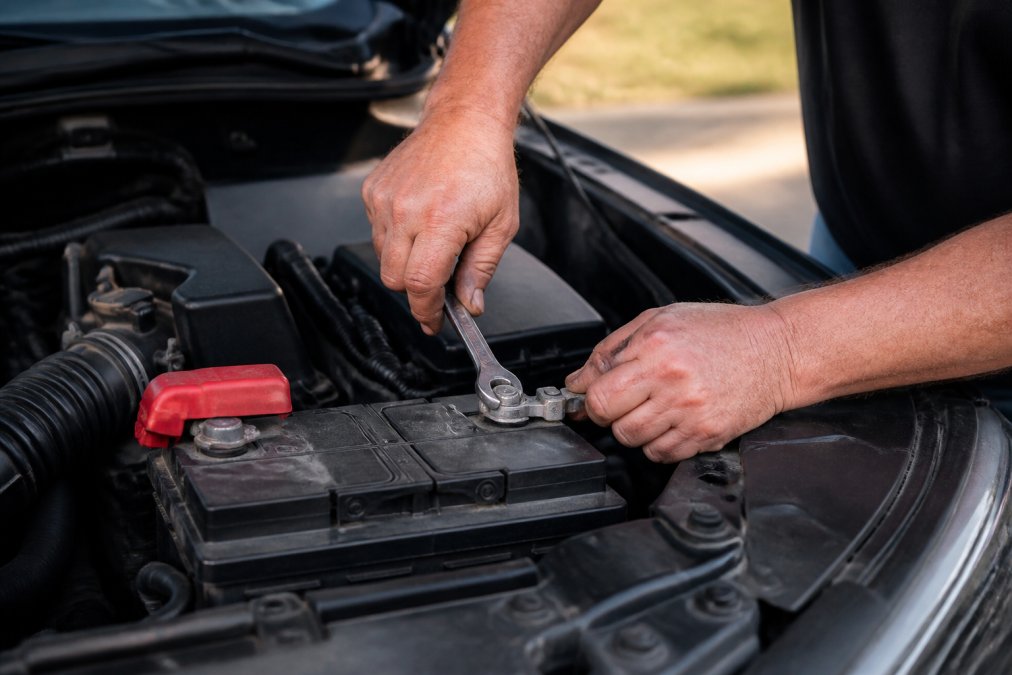 Mechanic using a wrench to disconnect the car battery to help reset car immobilizer system via power cycling.