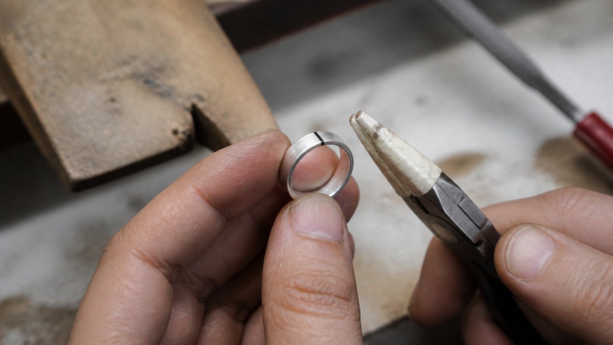 Hands holding a silver ring with taped pliers, marking the band for a precise DIY resizing adjustment process.