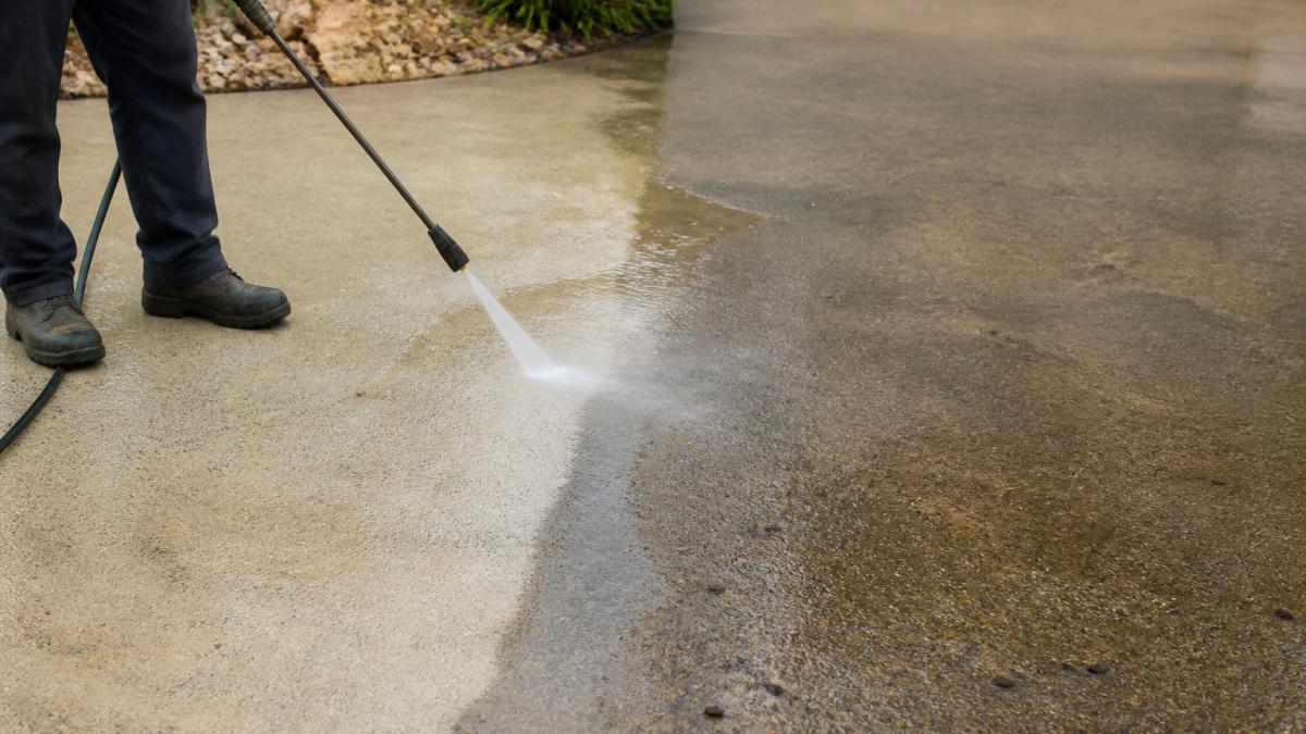 High-pressure water cleaning a driveway to restore faded concrete driveway surfaces by removing dirt and grime.