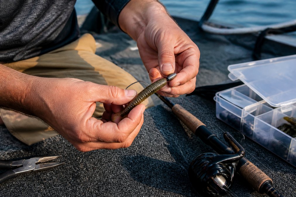 Hands threading a soft plastic lure onto a Texas rig hook to show how to rig bass fishing lures for beginners.