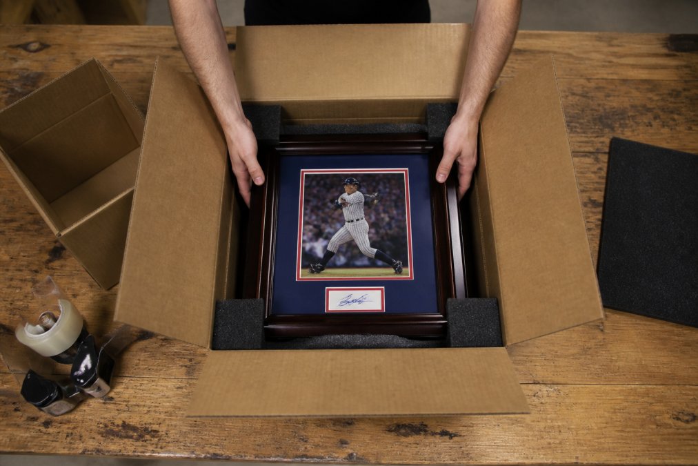 Placing a framed autographed collectible into a foam-lined outer box to safely ship expensive collectibles.