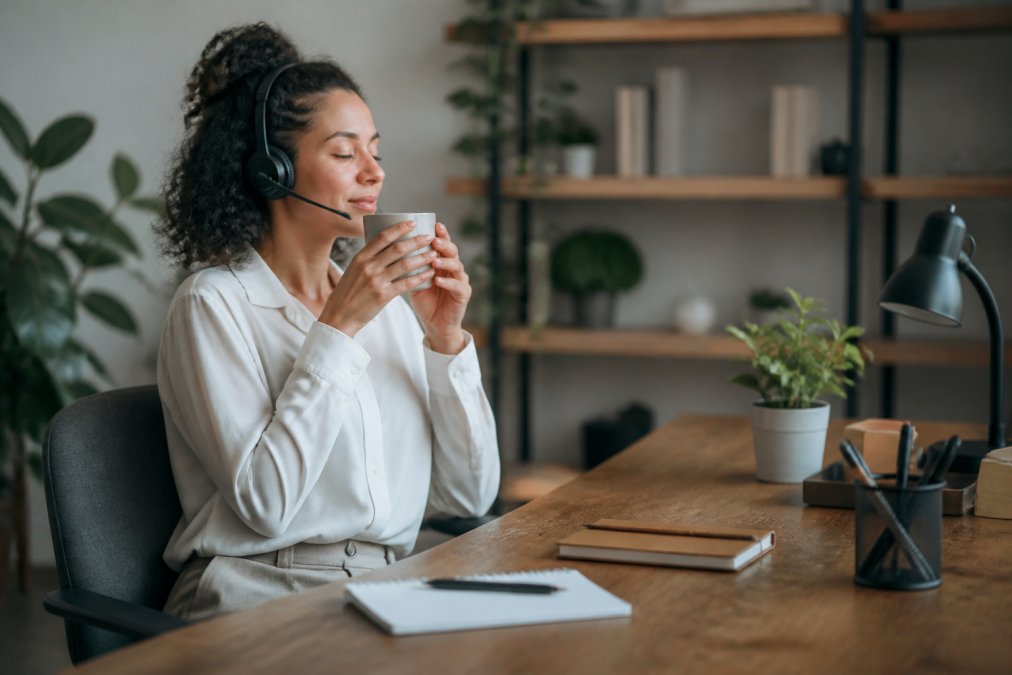 A customer service agent at their desk taking a mindful break, looking relaxed with a warm beverage, representing mental health and wellbeing in the workplace