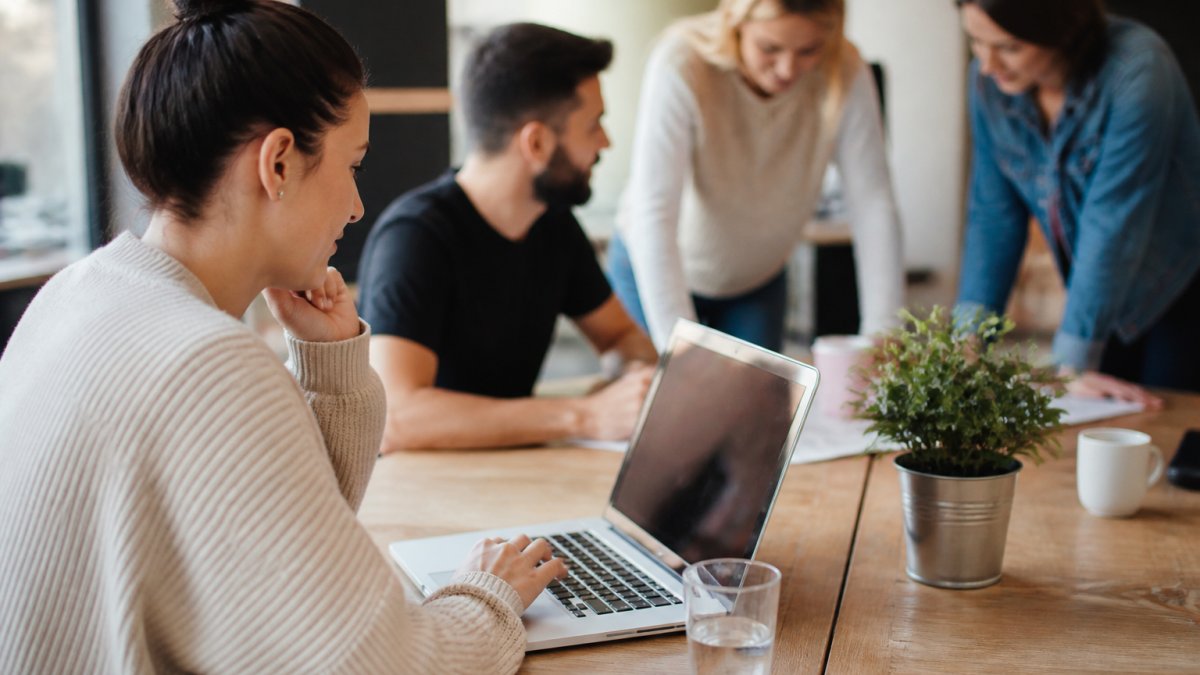 E-commerce manager reviewing store analytics and performance metrics on a laptop at a modern workspace, with team members collaborating on scaling strategy in the background