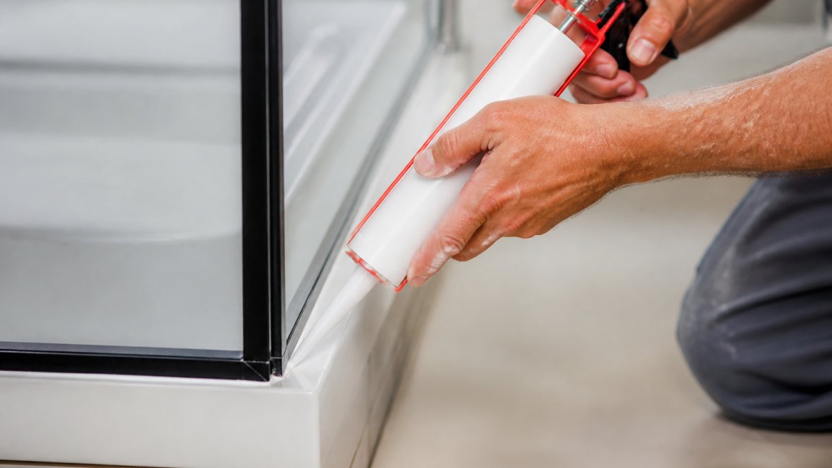 Professional applying silicone to seal bathroom shower enclosures with a caulking gun at a precise angle