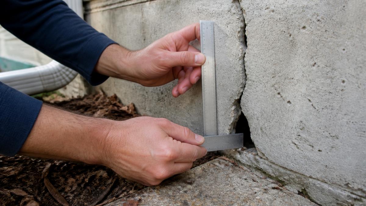 Homeowner measuring a crack in a foundation wall with a ruler, showing the depth and width of the opening