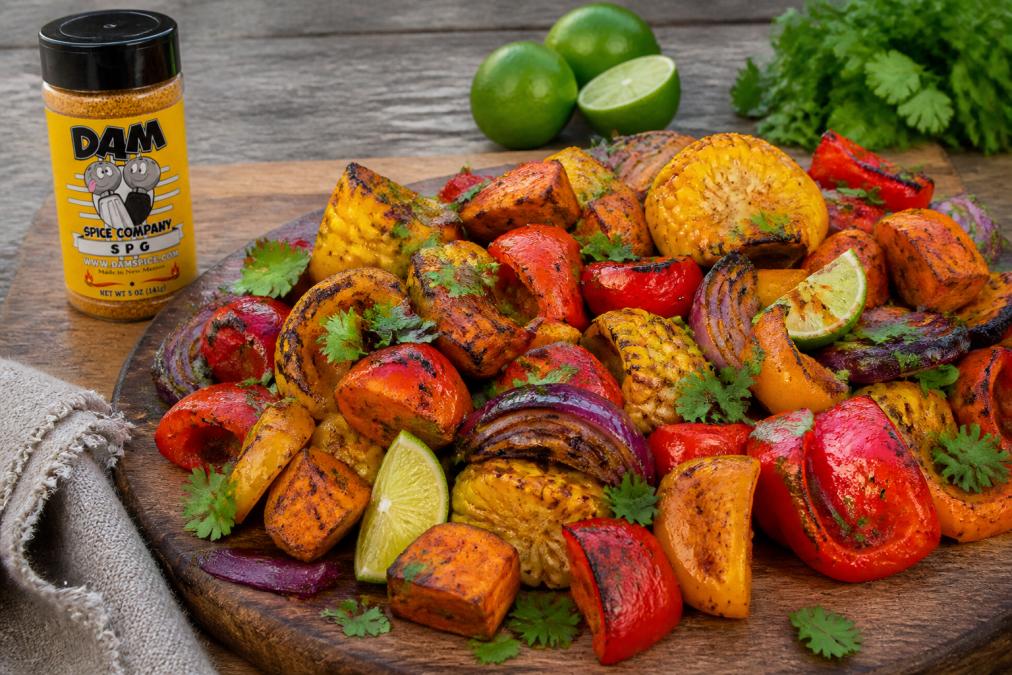A vibrant platter of roasted vegetables featuring charred bell peppers, caramelized sweet potatoes, and golden corn, seasoned with Southwest spices and garnished with fresh cilantro and lime wedges, served on a rustic wooden board
