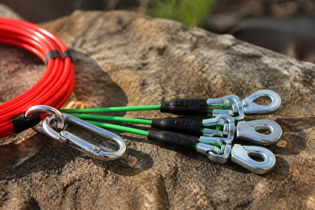 Close-up of a heavy-duty tie-out cable with swivel clips and carabiners attached, showing the hardware details and construction quality in natural daylight