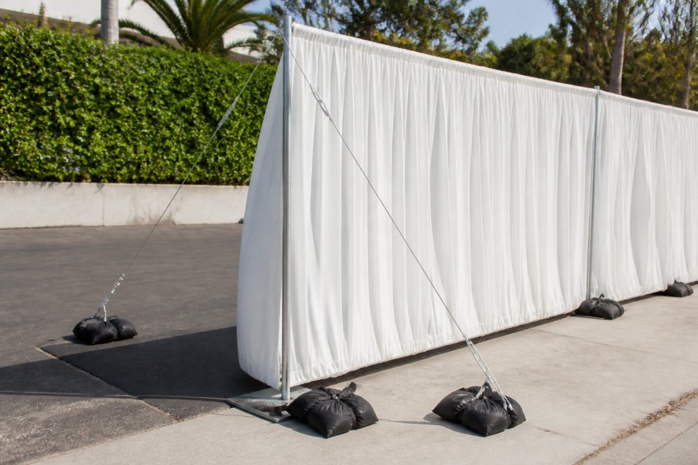 Outdoor event setup showing sandbags positioned at baseplate corners and guy wires attached to uprights at angles, demonstrating professional wind anchoring technique with clear anchoring points visible