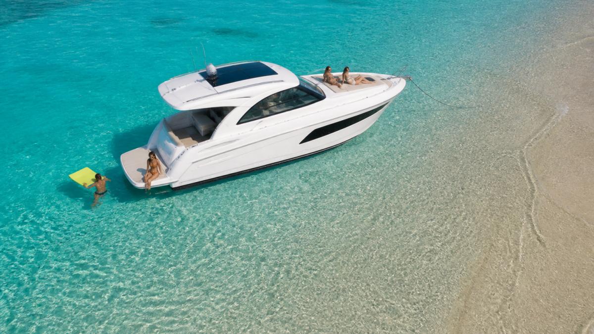 Aerial view of an express cruiser anchored at a sandbar with guests lounging on the bow and swim platform, clear turquoise water visible