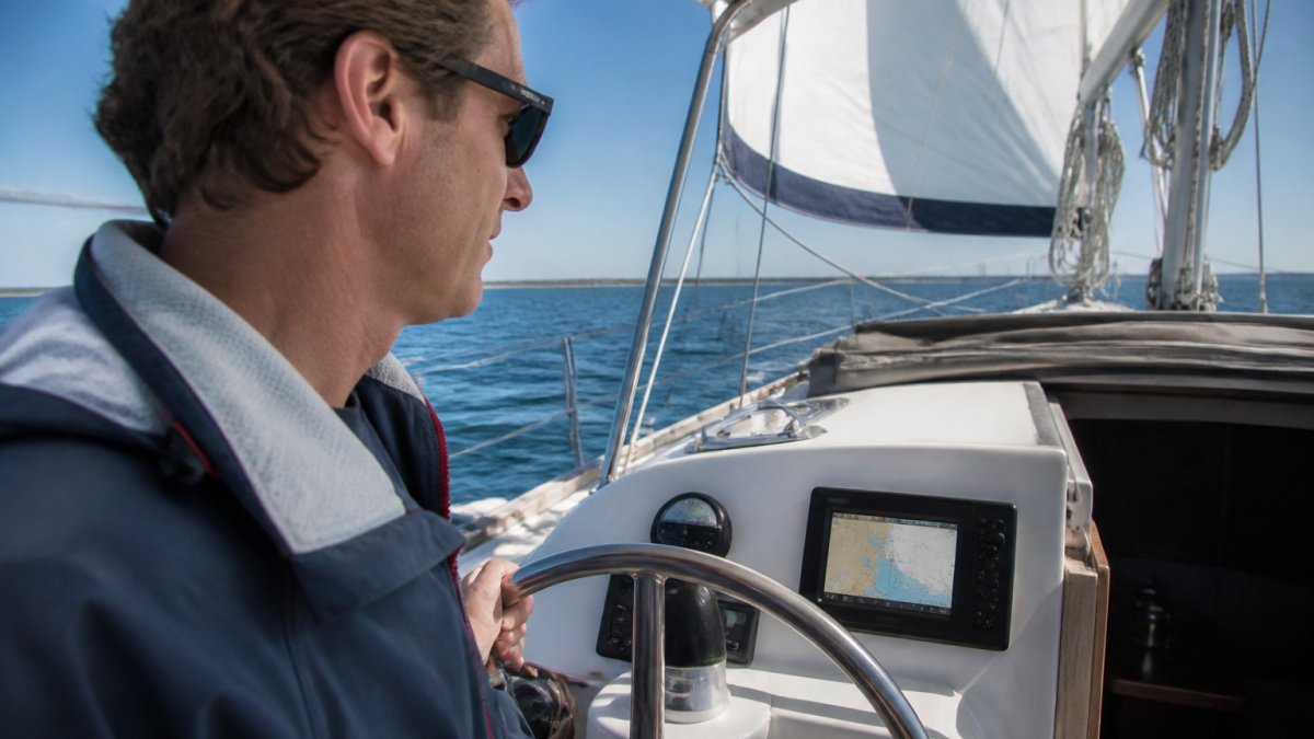 Sailor at the helm of a sailboat glancing at a 9-inch multifunction chartplotter screen mounted in the dash