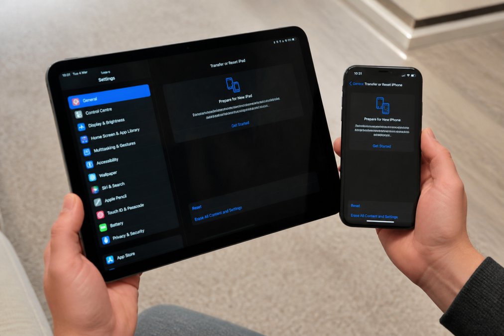 Close-up of hands holding a smartphone and tablet with settings screens visible, showing someone preparing devices for sale