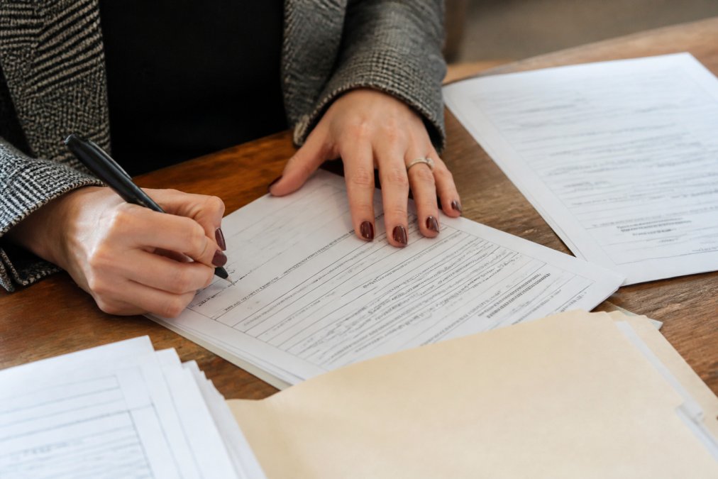 Close-up of hands completing legal paperwork at a desk with a pen, official Michigan court documents, and filing materials spread across the surface