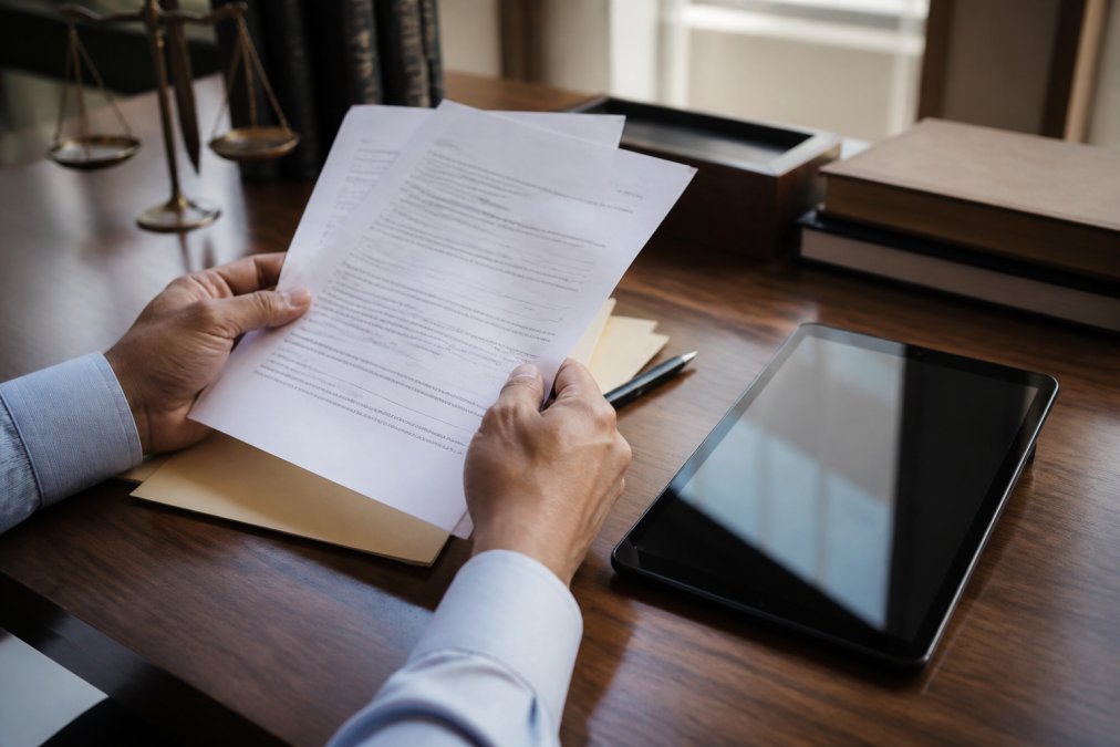 Close-up of hands holding printed court documents on a desk, with a digital tablet displaying a timestamped delivery confirmation screen placed beside them under natural office lighting