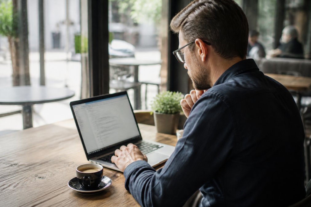 A small business owner reviewing website analytics on a laptop at a wooden desk in a modern cafe, coffee cup nearby, natural window light