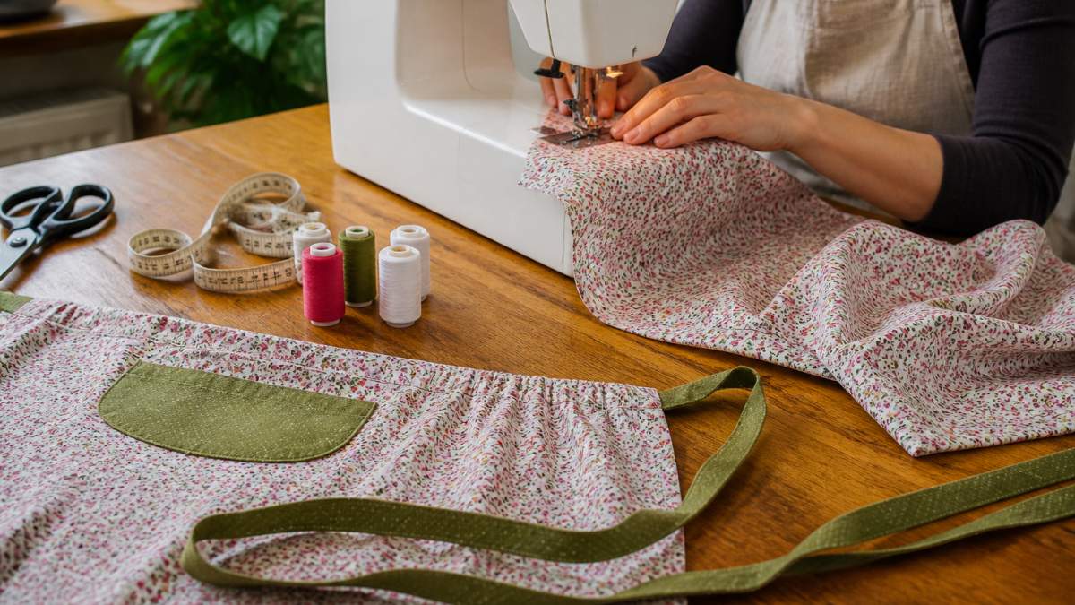 Hands stitching fabric on a sewing machine surrounded by scissors, measuring tape, and cotton cloth pieces