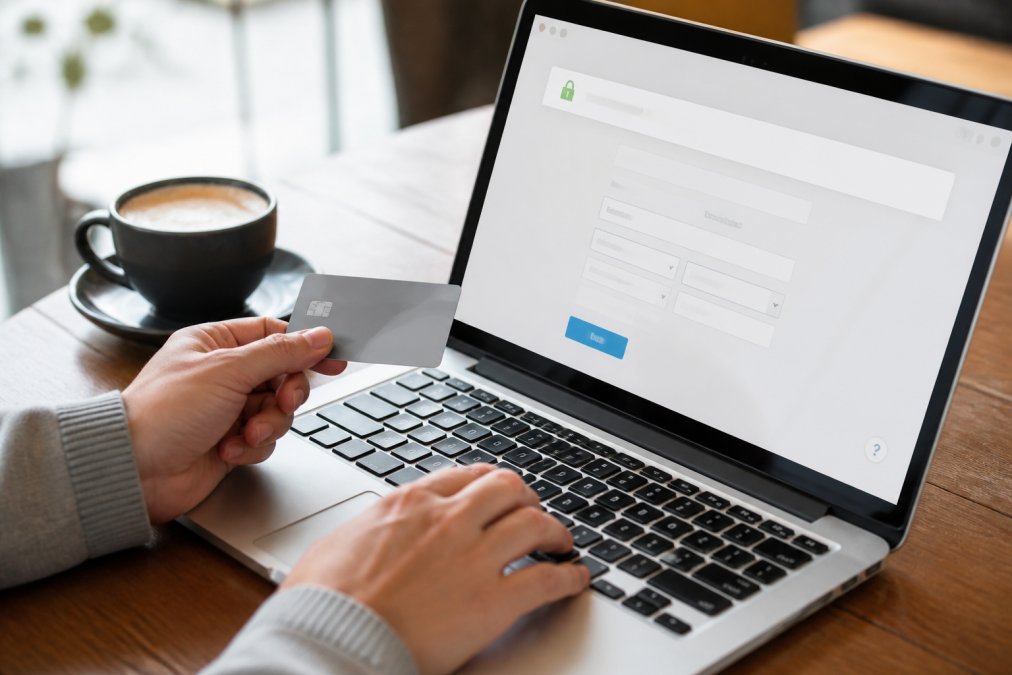 Close-up of hands entering payment information on a secure checkout page, with a padlock icon visible on the browser address bar and a coffee cup on the desk