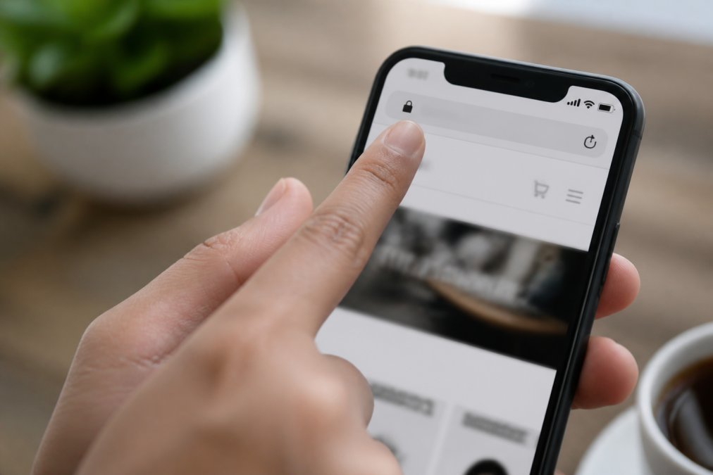 Close-up of a smartphone displaying a secure website with padlock icon in the address bar, person's hand pointing at the security indicator