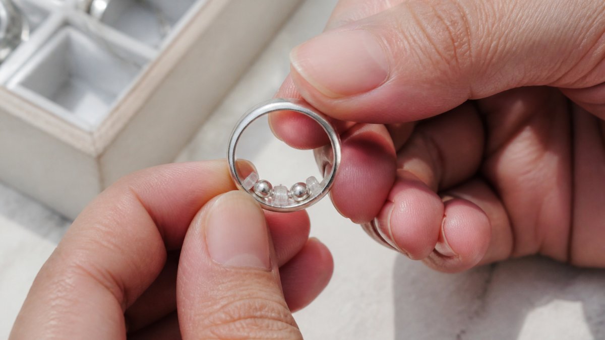 Close-up of hands holding a silver ring with sizing beads positioned inside the band, showing how the adjuster sits snugly on the inner circumference of the ring