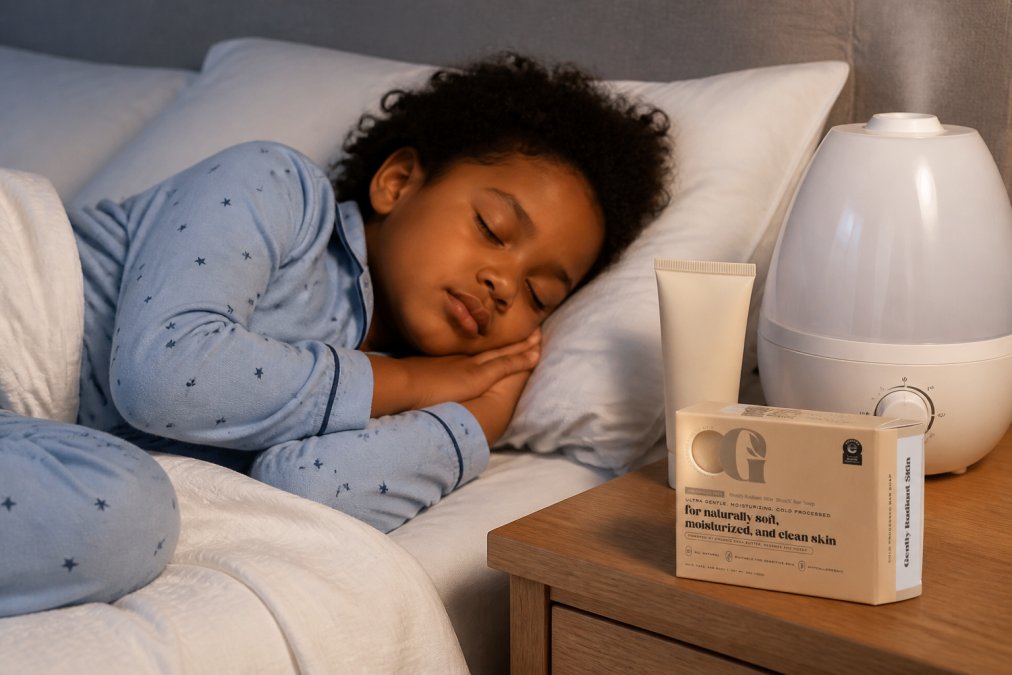 A child sleeping peacefully in soft, loose-fitting cotton pajamas, with a small humidifier visible on the nightstand and a tube of emollient cream nearby