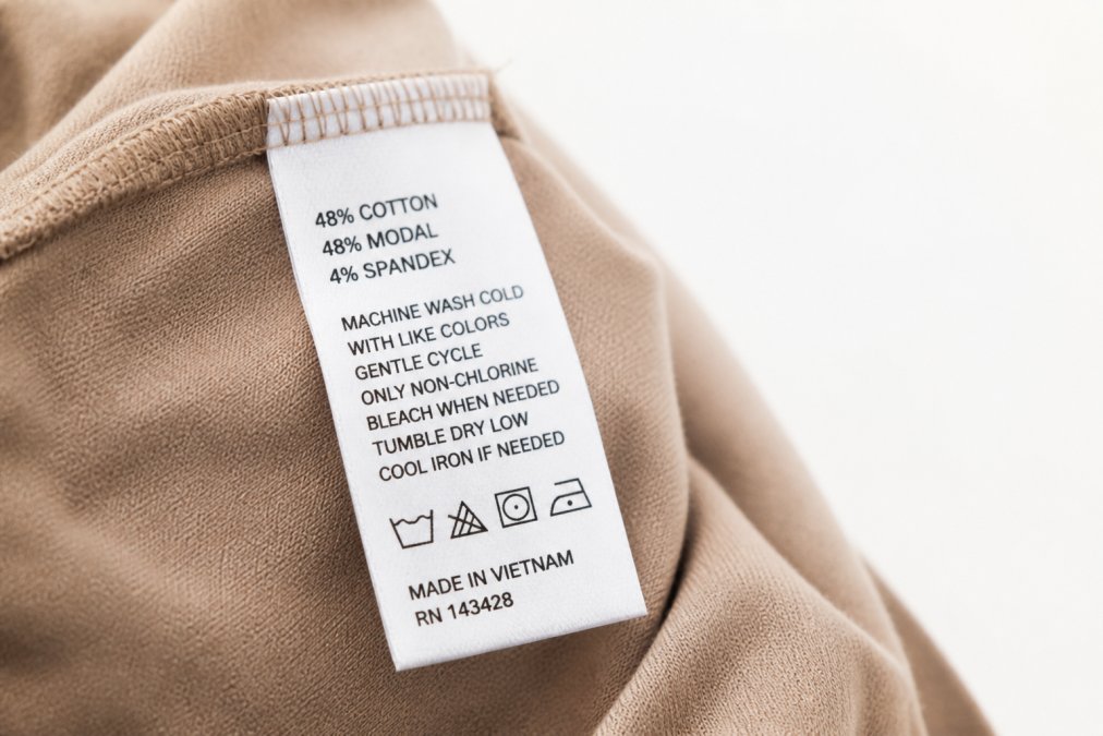 Close-up of a clothing label showing fiber content percentages, care instructions, and manufacturing details photographed against white background with natural lighting