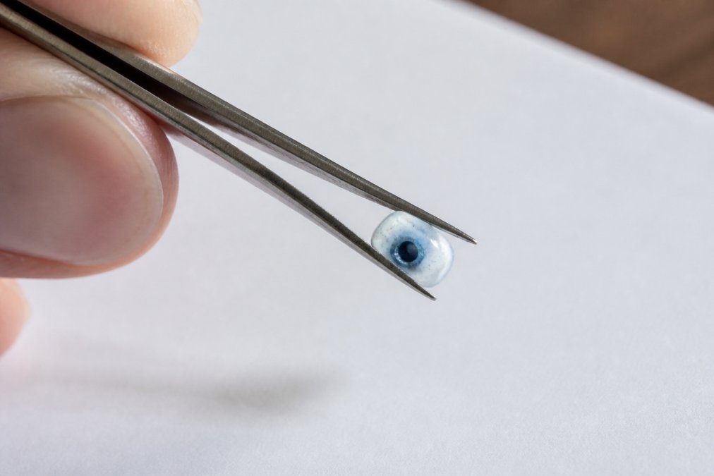 Extreme close-up of a crystal bead's drill hole showing concentrated dark blue dye residue against lighter stone, held by tweezers over a white surface