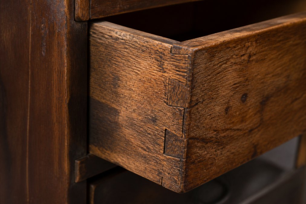 Close-up of antique wooden drawer showing hand-cut dovetail joints with visible saw marks, worn wood grain with checking patterns, and aged patina on interior surfaces